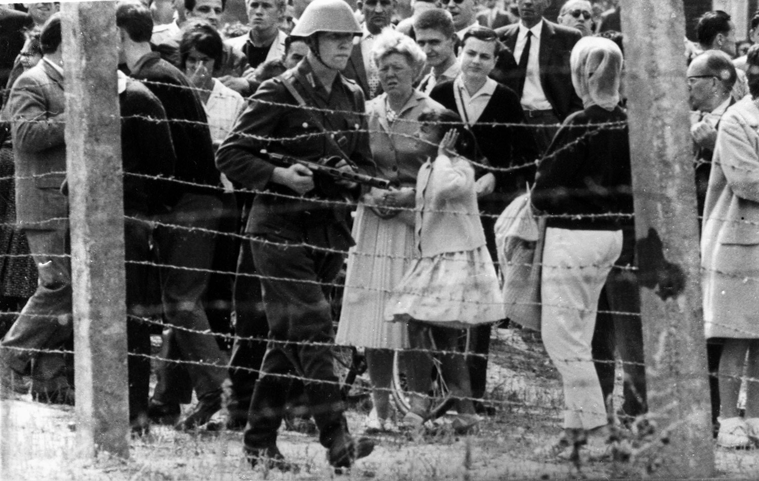 13. august 1961: Byggingen av Berlin-muren som skal skille Øst- og Vest-Berlin er i gang. Enkelte steder er det foreløpig bare en godt bevoktet piggtråd som deler Berlin. Her patruljerer en østtysk soldat med våpen langs et piggtrådgjerde på vesttysk side. 